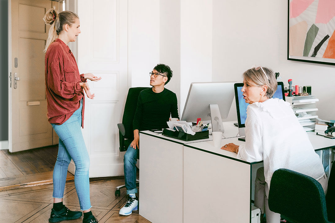 Group of three people around a desk talking.